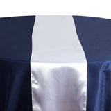 Elegant satin table runner on a navy tablecloth with plates and glassware. 