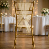 Elegant gold chiavari chair with a cream bow, set for a wedding reception.