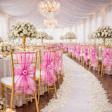 Elegant wedding reception with gold chairs and pink sashes, decorated with floral arrangements.
