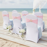Elegant white wedding chairs with pink sashes on a beach setting.