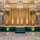 Elegant event stage with gold curtains, chandeliers, and greenery decorations.