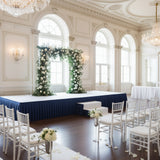 Elegant wedding ceremony setup with floral arch and white chairs.