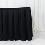 Black pleated table skirt on white floor with draped backdrop