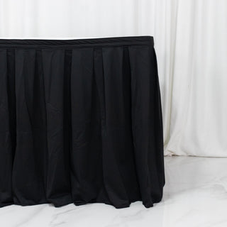 Black pleated table skirt on white floor with draped backdrop