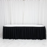 Black skirted banquet table with white top against white curtains