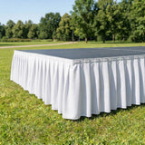 White outdoor event table with pleated table skirt on grass in park
