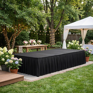 Outdoor garden event with stage, string lights, flowers, and white canopy tent