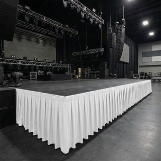 Empty concert stage with rigging, speakers, and white skirting in event venue