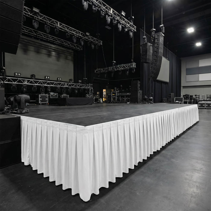 Empty concert stage with rigging, speakers, and white skirting in event venue