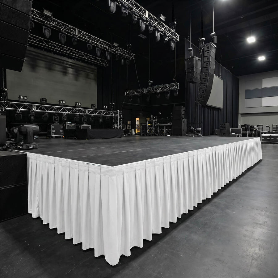 Empty concert stage with rigging, speakers, and white skirting in event venue