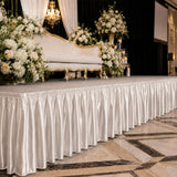 Elegant wedding stage with white flowers, gold sofa, and satin draped table skirting
