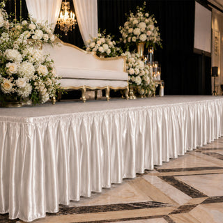 Elegant wedding stage with white flowers, gold sofa, and satin draped table skirting