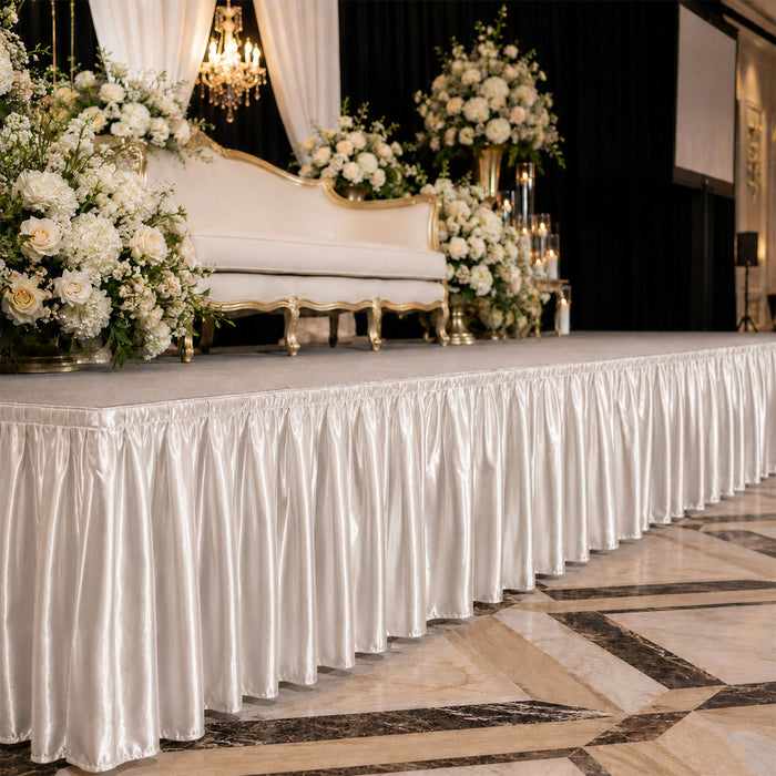 Elegant wedding stage with white flowers, gold sofa, and satin draped table skirting