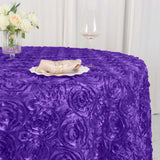 Purple rose-patterned tablecloth draped over a table with a glass and floral centerpiece.