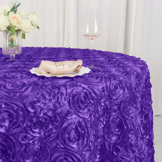 Purple rose-patterned tablecloth draped over a table with a glass and floral centerpiece.
