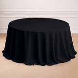 Black round tablecloth on a wooden floor in a styled setting.