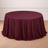 Burgundy round tablecloth with elegant draping on a wooden floor.