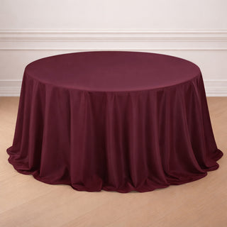 Burgundy round tablecloth with elegant draping on a wooden floor.