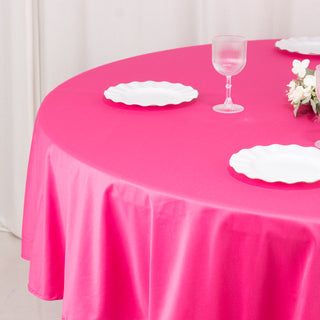 Pink tablecloth with white plates and a glass on a round table.