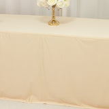 Beige tablecloth draped over a table with a gold candlestick and white roses.
