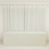 White table cover on a plain table with sheer white curtains in the background.