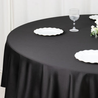 Black tablecloth draped over a round table with white plates and a glass.