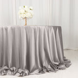 Silver satin tablecloth draping elegantly on a round table with floral centerpiece.