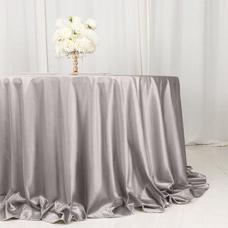 Silver satin tablecloth draping elegantly on a round table with floral centerpiece.