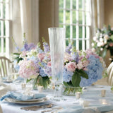Elegant tall crystal vase surrounded by pastel floral arrangements on a dining table.