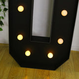 Black marquee letter "U" with glowing bulbs on a wooden floor.