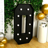 Black marquee letter "O" with bulbs, set against greenery and balloons.