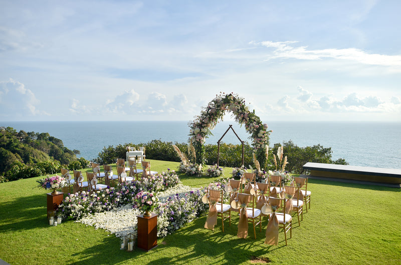 Outdoor wedding ceremony setup with floral arch and ocean view