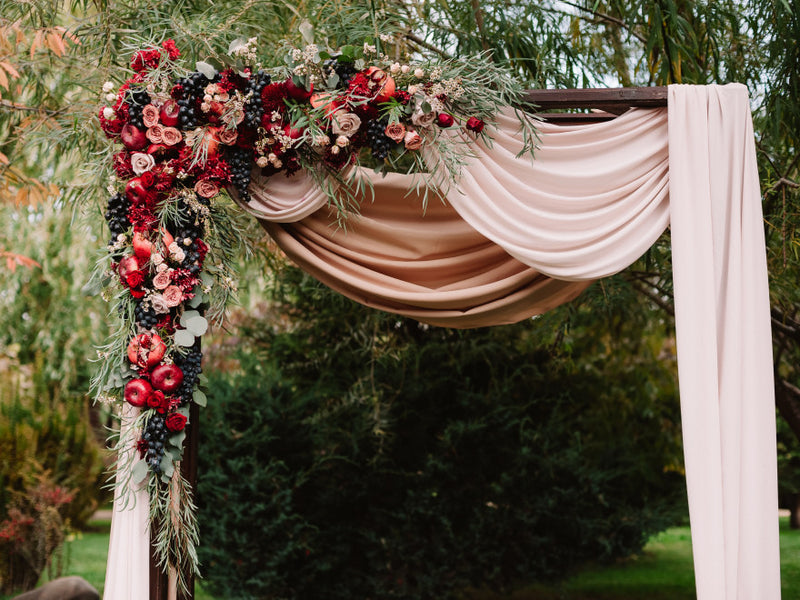 Floral wedding arch with draped blush and taupe fabric