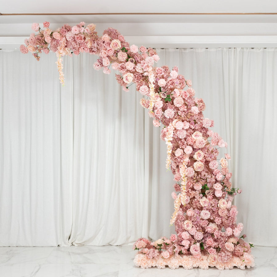 Floral arch made of pink roses and peonies against a white backdrop.