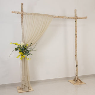 Wooden arch with draped fabric and floral arrangement, set against a plain background.