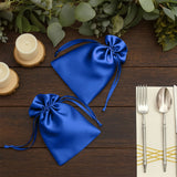 Blue satin favor bags on a wooden table with candles and silverware.