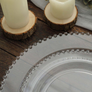 Clear decorative plate with beaded rim next to candles on wooden table.