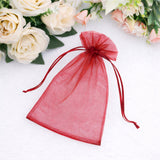 Red organza gift bag with drawstring closure against floral background.