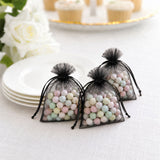 Pastel candy balls in black organza gift bags on a white table