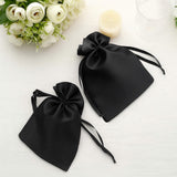 Two black satin drawstring bags on a light surface with flowers and a candle.