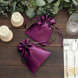 Purple satin gift bags on a rustic wooden table with candles and greenery.