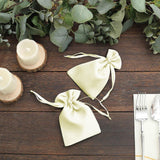 Two elegant ivory drawstring bags on a rustic wooden table with candles and greenery.