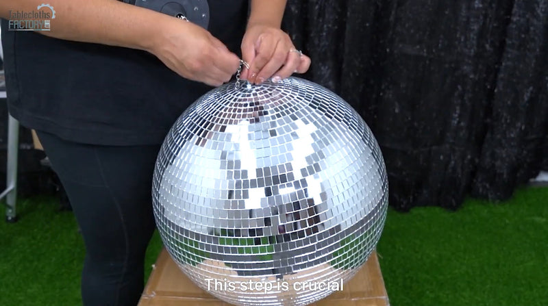 Hands attaching a chain securely to a disco ball for hanging.