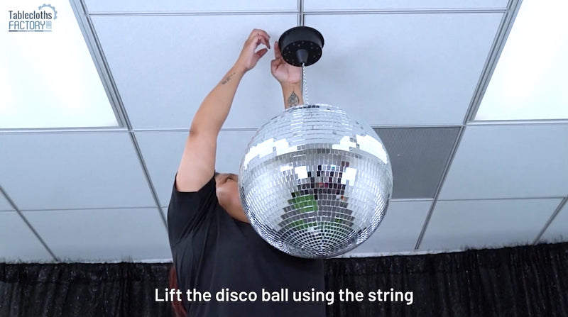 Person lifting a disco ball to attach it securely to the ceiling mount.