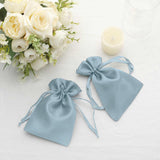 Blue satin drawstring bags with floral arrangement and candle in the background.