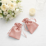 Two pink satin drawstring bags on a table with flowers and a candle.