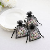 Black organza gift bags with pastel candy balls on a white table￼