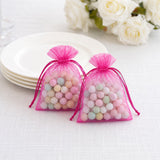 Pink organza drawstring gift bags with pastel candy beads on a white table