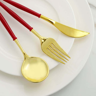 Gold cutlery set with red handles on a white plate.