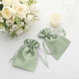 Two elegant green satin drawstring bags on a table with flowers and a candle.
